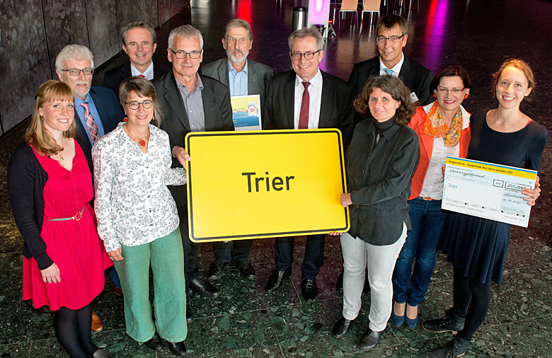 Eine Gruppe, die das Ortsnamensschild Trier trägt, lächelt in die Kamera.